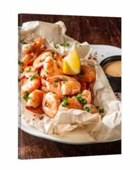 Cooked shrimp served on parchment with creamy dipping sauce, lemon wedge, parsley garnish, and red pepper flakes. Clean, appetizing seafood presentation on white plate.