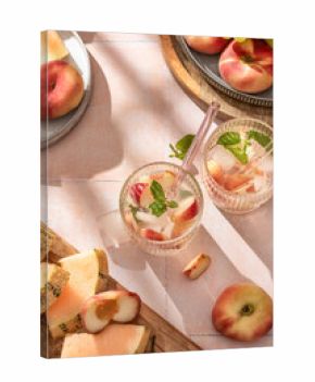 Summer cold drinks: homemade iced peach lemonade with mint in glass on pink tile background in bright morning light, top view