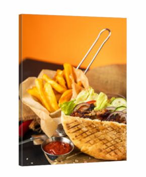 Grilled pita sandwich with fries and ketchup on wooden board, vibrant orange background