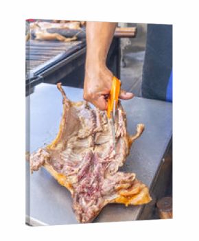 Person cutting roasted guinea pig with kitchen scissors on a metal table, a typical Andean dish from Ecuador. Traditional gastronomic scene reflecting culture and authentic flavors of the Andes.