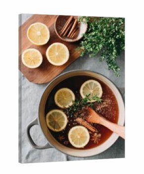 A person stirs a pot of spiced apple cider filled with sliced lemons, cinnamon sticks, and herbs. The cozy kitchen evokes warmth and comfort during the fall season