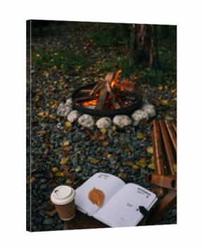 Cozy autumn scene with a campfire, coffee, and a journal in the forest