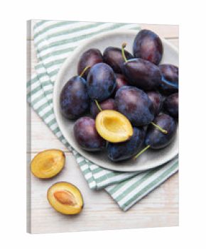 Fresh ripe plums in grey bowl on wood table
