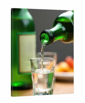Person pours clear korean soju liquor from green bottle into small glass. Alcohol beverage being served for consumption in bar or restaurant.