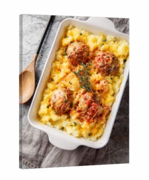 Meatball casserole with mashed potatoes, cheese, tomato sauce, and thyme in a baking dish on the table. Vertical top view from above
