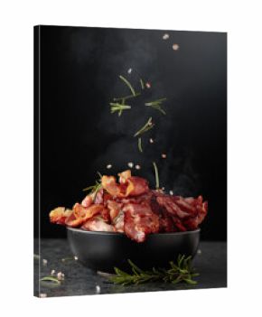 Fried bacon in a black dish, sprinkled with rosemary and pink salt.