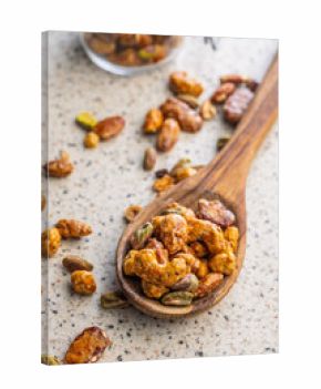 Nuts coated in sugar glaze on wooden spoon on kitchen table.