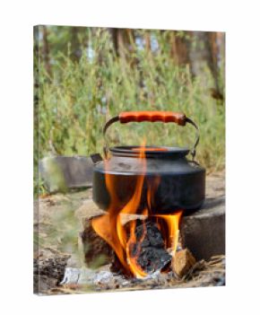 black camping kettle heating on fire in nature, vertical frame