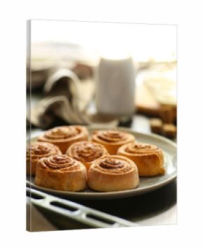 Plate with tasty baked cinnamon rolls on table in kitchen