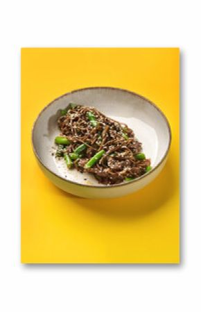 Soba noodles with beef and green onions on vibrant yellow background
