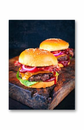 Classical cheeseburger with beef patty, cheese and bacon served as close-up with onion rings and tomato ketchup on a wooden cutting board