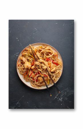 Delicious udon noodles stir fried with chicken meat and vegetables, sprinkled with sesame seeds, served on a plate with chopsticks on a dark background, creating an appetizing asian cuisine scene