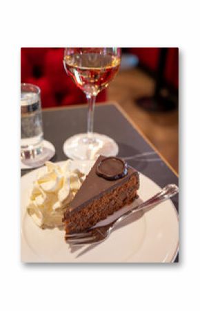 Piece of famous Sachertorte chocolate cake with apricot jam of Austrian origin served with whipped cream in old classic cafe-restaurant in Vienna