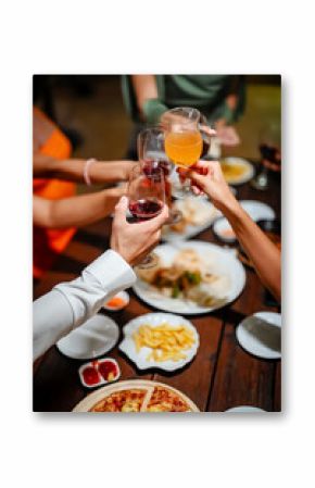 Close-up of friends sharing a delicious meal and drinks at a lively dinner party, featuring seafood, fries, and wine on a wooden table