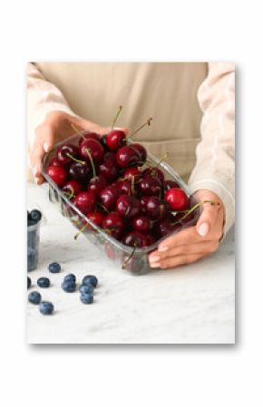 Woman holding plastic container with ripe cherries at table
