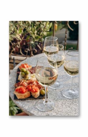 Outdoor dining or aperitif white wine glasses on a stone table with gourmet charcuterie board assorted meats, olives, and cheese