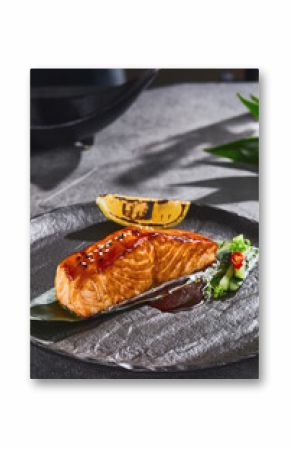 Miso-glazed salmon steak with sesame seeds in bright rustic lighting, closeup presentation on textured black plate