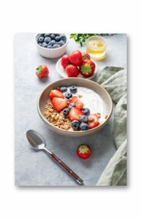 Natural yogurt with granola, blueberry and strawberry in a bowl on a light background