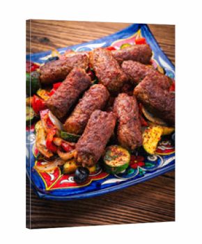Traditional Croatian cevapi spicy meat ball rolls with troasted vegetables served as close-up on rustic design plate