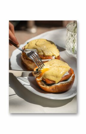 Eating eggs benedict with salmon on brioche bun in sunlight
