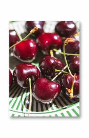 Close-up of fresh dark red cherries with stems on a decorative green striped plate, captured in natural sunlight with vibrant detail and summery freshness.