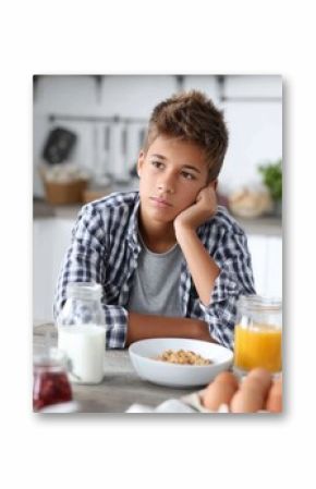 Pensive hispanic teen boy sitting at breakfast table with milk and juice in a kitchen setting.