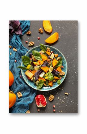 Plate of delicious salad with persimmon, pomegranate seeds and walnut on black background
