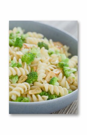 Fusilli or rotini pasta with broccoli, roasted garlic slices, herbs and olive oil, served in blue bowl (Selective Focus, Focus one third into the dish)