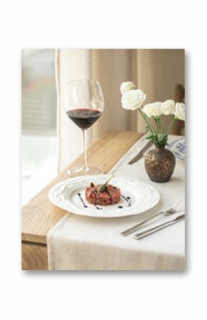 Beef tartare with caper and balsamic sauce on white plate with wine