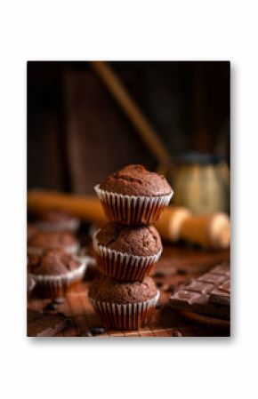 Chocolate muffins with liquid chocolate and dulce de leche with cocoa powder, a chocolate bar, and coffee beans on a wooden table with kitchen utensils.