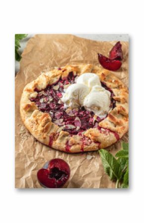 French Galette or pie with plums and almonds served with ice cream scoops on parchment paper background. Summer traditional homemade sweet pastries