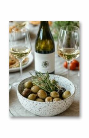 Still life with bottle of white wine, two glasses, and bowl of olives on marble, creating an elegant Mediterranean dining or tasting invitation.