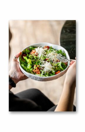 Close-up of a person holding a bowl of fresh salad with lettuce, cherry tomatoes, shredded cheese, and a fork, representing healthy eating and vibrant food textures.