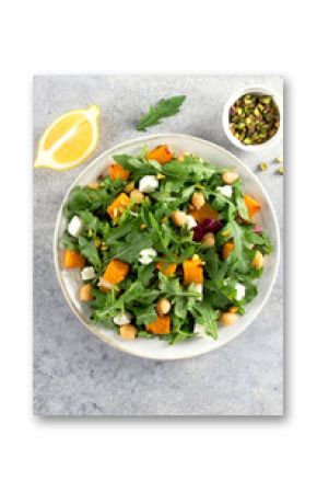 Healthy arugula salad with roasted pumpkin, chickpeas, feta cheese, pistachios on gray background.