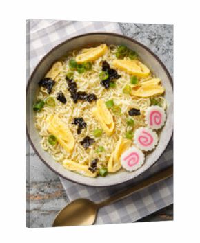Saimin is a Hawaiian noodle soup consisting of soft wheat egg noodles served in a hot dashi garnished with diced green onions, kamaboko and omelette closeup in the plate. Vertical top view from above
