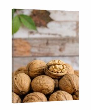 Close-up view of a pile of walnuts, showcasing their rich brown hues and textured shells, with one walnut cracked open to reveal the light-colored kernel inside.