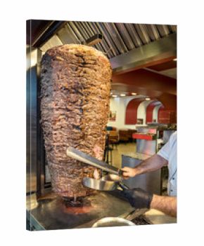 Close up of a huge spinning meat top called in Turkish “Doner Kebab”. Slicing lamb or beef meat from the rotating heap of stacked and broiled meat.