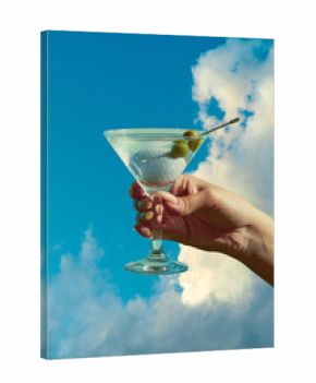 Hand holding martini glass with olives and golf ball against blue sky stylish surreal mood. Concept of creative advertising, lifestyle branding, sports culture and cocktail promotion.