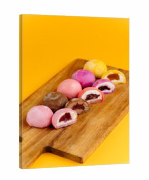 Assorted mochi ice cream on wooden board over vibrant yellow background, flat lay