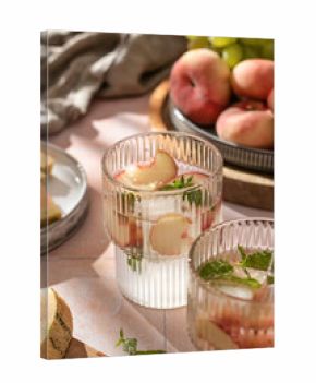 Summer cold drinks: homemade iced peach lemonade with mint in glass on pink tile background in bright morning light