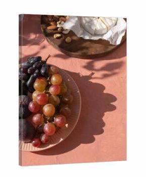 Plate with ripe figs fruit, bunches of grapes, brie cheese and nuts on the mediterranean pink terracotta color plaster background with leaves shadows.