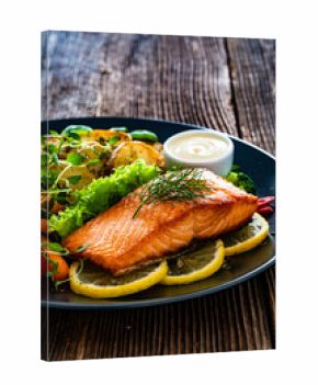 Fried salmon steak with boiled broccoli and mini carrots, fried potatoes and mayonnaise on wooden table 