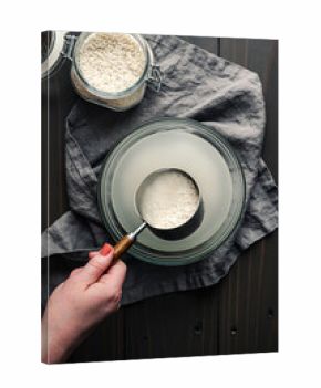 Hand Holding a Measuring Cup of Soaking Sticky Rice: Scoop of glutinous rice held over a glass bowl full of cloudy water and soaked sweet rice