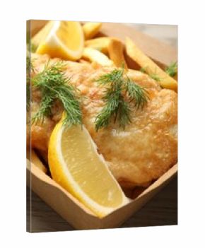 British Traditional Fish and chips with lemon in paper box on wooden table, closeup
