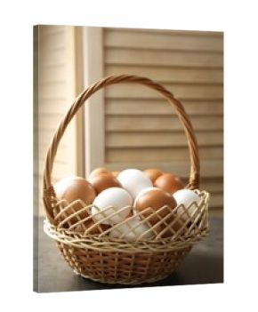Raw chicken eggs in wicker basket on grey table