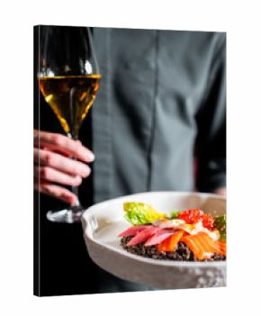 A person holds a gourmet seafood dish with salmon, tuna, quinoa, and roe, and a wine glass. Fine dining, restaurant, and luxury concepts are highlighted