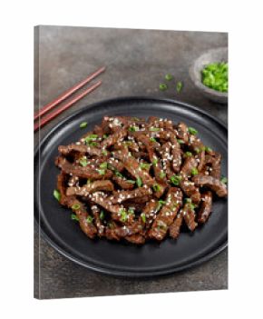 Fried teriyaki beef with sesame seeds and green onions on a brown background. Asian cuisine.