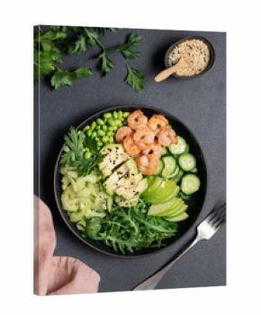 Healthy green shrimp salad with avocado, celery, apple, arugula, edamame beans, cucumber, and parsley in black bowl on dark background, top view