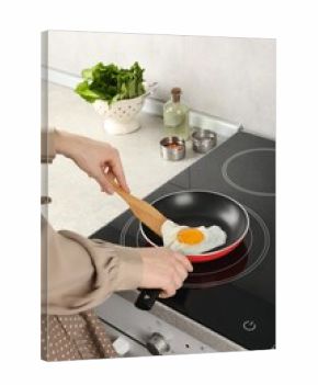 Woman taking fried egg with wooden spatula in kitchen, closeup