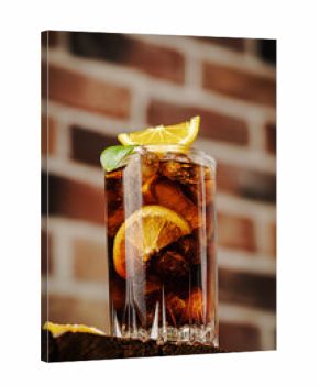 Cuba Libre in a glass with brown rum, cola, mint and lemon on brick background. Cuba Libre or long island iced tea cocktail with strong drinks